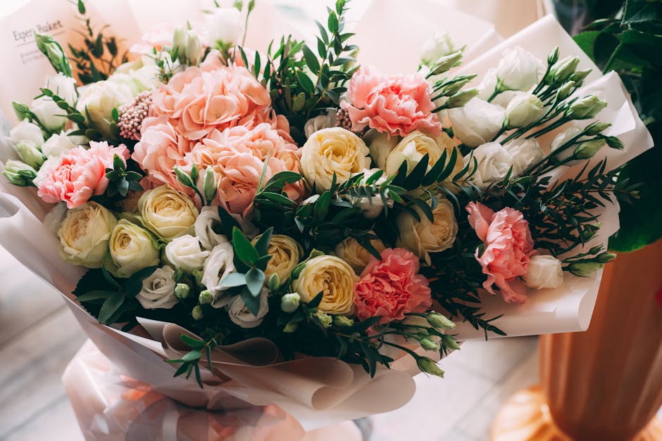 A beautifully arranged bouquet of fresh flowers featuring soft pink hydrangeas, creamy white roses, and delicate white lisianthus, complemented by green foliage with glossy leaves and fern-like stems.