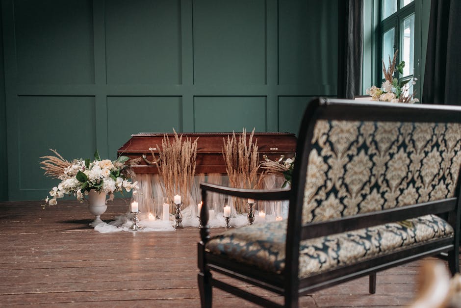 A floral arrangement featuring white roses, hydrangeas, and greenery in a white ceramic vase is placed on a dark wooden table, accompanied by tall, feathery pampas grass in a matching vase. Small whit